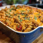 Baked cheesy taco pasta casserole with beef, garnished with cheese and herbs
